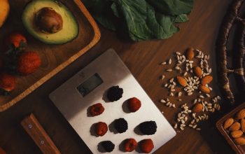 Top view of composed raw almond with seeds and avocado on table with berries on scales for cooking healthy dish