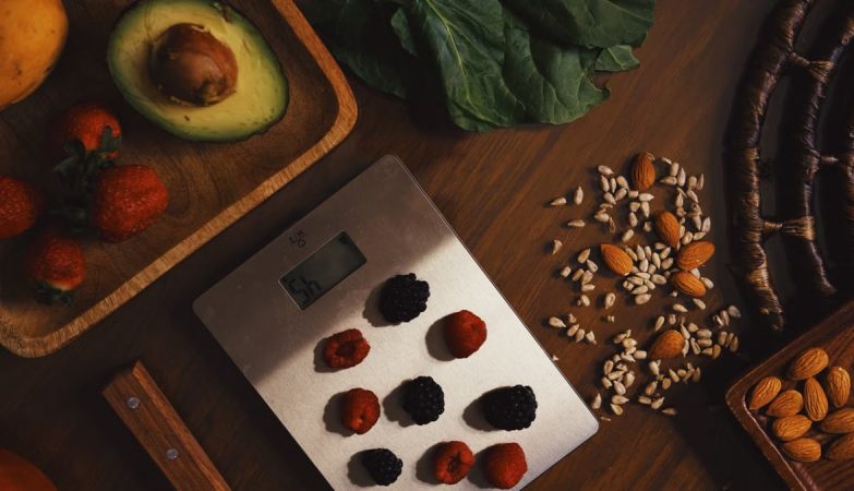 Top view of composed raw almond with seeds and avocado on table with berries on scales for cooking healthy dish