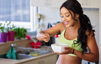 Cheerful woman enjoying fresh strawberries in a cozy kitchen setting. Promotes healthy living and happiness.